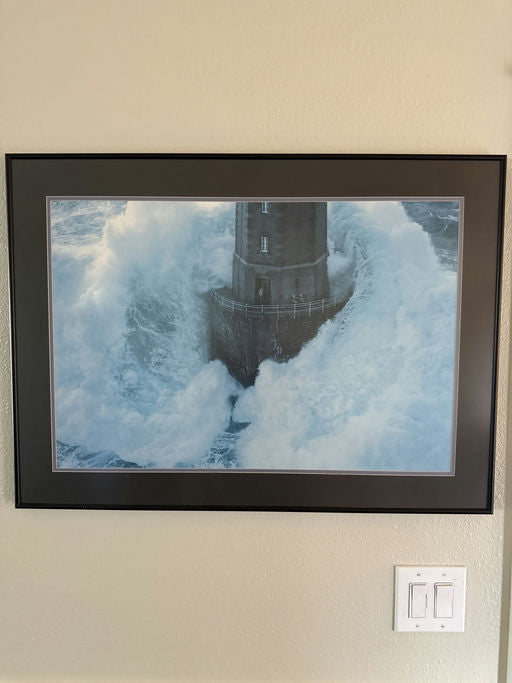 A lighthouse stands resilient amidst crashing waves, surrounded by turbulent seas, capturing the raw power of nature in a dramatic coastal scene.