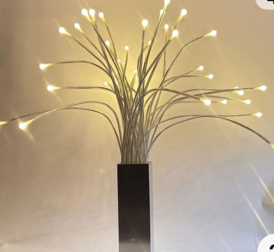 A decorative LED lamp with multiple light strands resembling a plant, producing a warm glow against a neutral background.