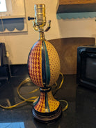 A colorful, decorative lamp shaped like an egg, featuring multicolored patterns and a brass socket on top, placed on a dark countertop.