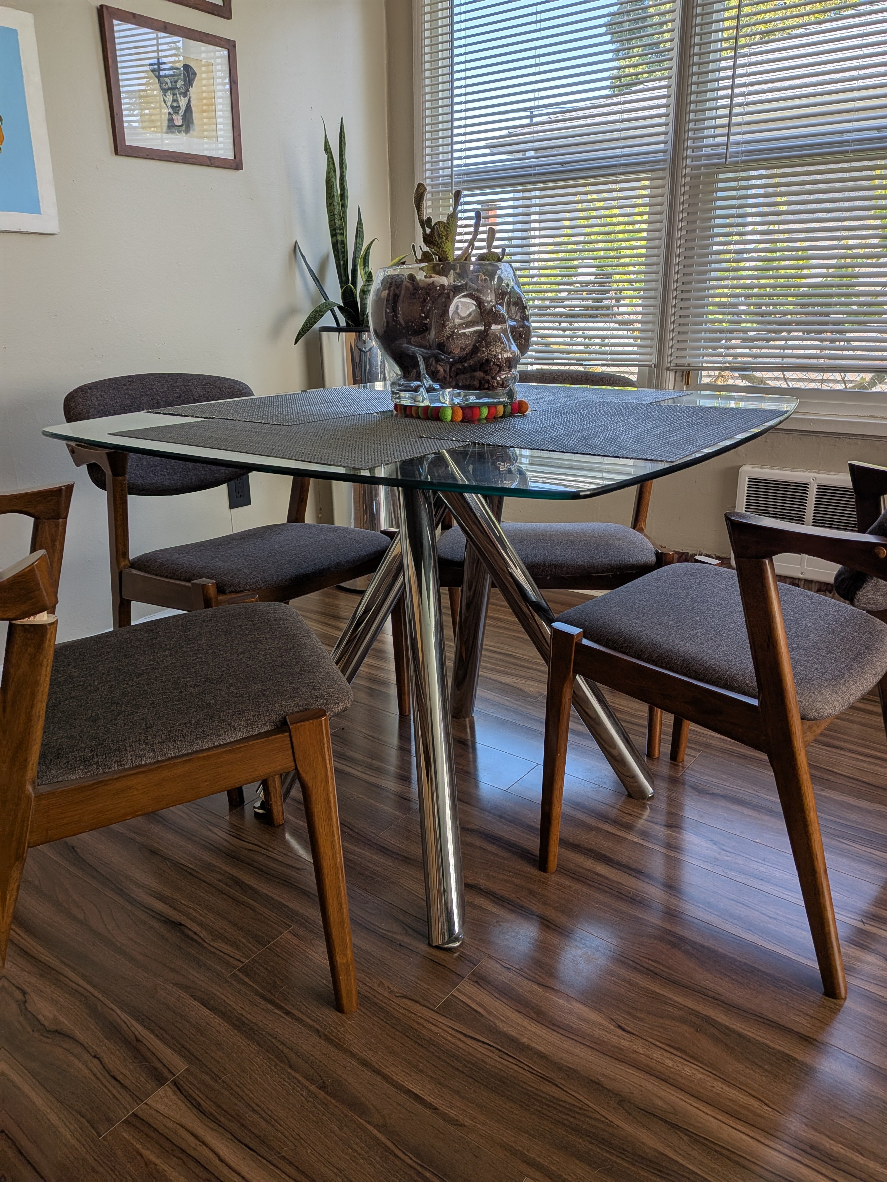 A modern dining area with a glass-top table supported by chrome legs, surrounded by wooden chairs. A decorative glass skull holds plants.